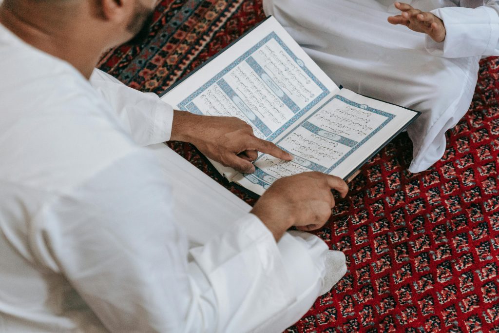 Close-up of two people studying the Quran on a patterned carpet. Religious education setting.